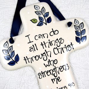 May include: White ceramic cross with blue and gray floral designs. The cross has the text "I can do all things through Christ who strengthens me" and the scripture reference "Philippians 4:13".