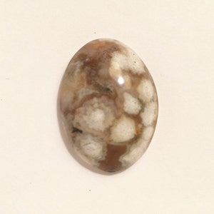 May include: A white and brown agate cabochon with a unique pattern. The stone is oval shaped and has a smooth, polished surface.