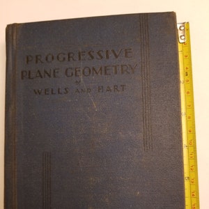Puede incluir: Un libro de tapa dura azul titulado "Progressive Plane Geometry" de Wells y Hart. El libro forma parte de la serie Wells-Hart Mathematics.