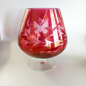 以下が含まれることがあります： 蝶の模様がエッチングされた赤いガラスのデカンタ。デカンタは丸いボディと透明なガラスのベースを持っています。