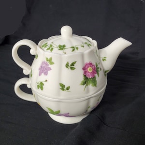 May include: A white porcelain teapot with a floral design. The teapot has a lid and a handle. The teapot is decorated with pink, purple, and green flowers.