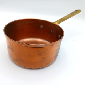 以下が含まれることがあります： 真鍮のハンドルが付いた銅製のソースパン。鍋は丸みを帯びた形状で、少し古びた外観をしています。ハンドルはリベットで取り付けられています。鍋の内側はより濃い銅色です。