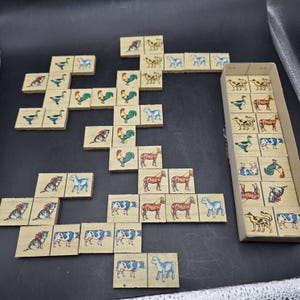 May include: A vintage set of wooden dominoes with illustrations of farm animals, including horses, cows, and roosters. The dominoes are arranged on a dark surface, some in a box. The illustrations are in brown, blue, and red.