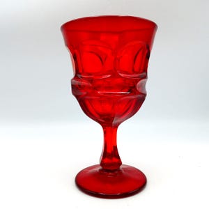 Puede incluir: Un vibrante cáliz de vidrio rojo con un diseño detallado y texturizado. El cáliz presenta un cuenco redondeado con un exterior estampado, un tallo delgado y una base circular. El vidrio es transparente, permitiendo el paso de la luz, sobre un fondo blanco.
