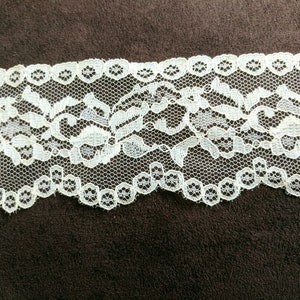 May include: White lace trim with a delicate floral pattern. The lace has a scalloped edge.