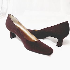 May include: A pair of brown suede heeled pumps with a square toe. The heels are a low block style.