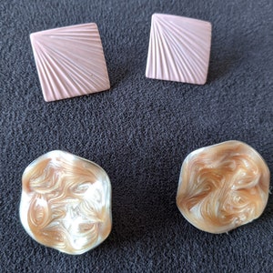 May include: Four decorative buttons in a variety of shapes and colors. Two are square and pink with a sunburst design. Two are round and have a swirling pattern in shades of brown and white.