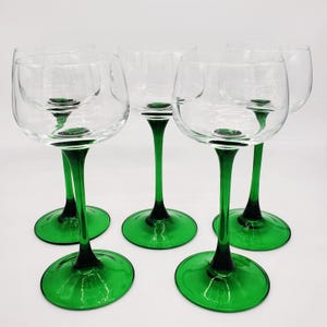 Puede incluir: Juego de cinco copas de vino transparentes con tallos y bases verdes. Las copas tienen forma de cuenco redondeado. El color verde añade un toque de color a la elegante cristalería. Cada copa mide unos 20 cm de alto.