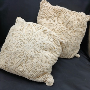 Puede incluir: Dos cojines de crochet de color crema con un delicado patrón floral.
