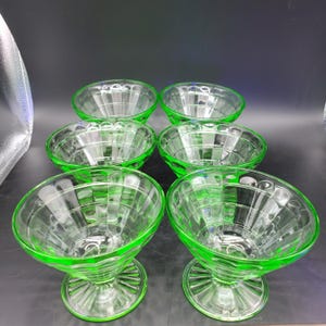 Könnte beinhalten: Sechs grüne Glasschalen für Desserts mit geriffeltem Design. Die Schalen haben einen Sockel und eignen sich perfekt zum Servieren von Eis, Pudding oder anderen Desserts.