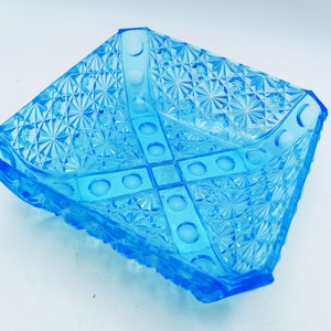 Könnte beinhalten: Eine quadratische, hellblaue Glasschale mit einem strukturierten, geometrischen Muster. Die Schale hat ein kreuzförmiges Design in der Mitte und einen gewellten Rand. Die Schale ist wahrscheinlich Vintage und eignet sich zum Servieren von Snacks oder zum Präsentieren kleiner Gegenstände.