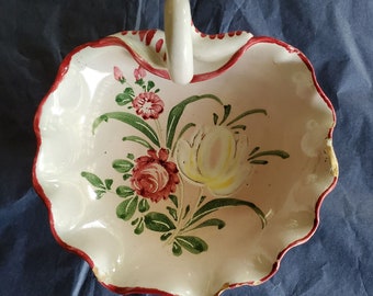 May include: A white ceramic bowl with a red rim and a handle. The bowl is decorated with hand-painted flowers in shades of pink, red, and green.