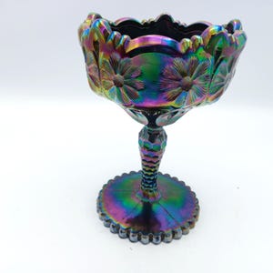 Puede incluir: Cuenco de pedestal de vidrio iridiscente con diseño floral. El cuenco tiene un borde festoneado y una base redonda. El tallo tiene un patrón de panal. Los colores cambian de morado a verde y azul.