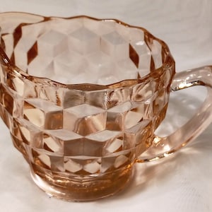 Könnte beinhalten: Ein rosa gläserner Milchkännchen mit einem Diamantenmuster. Der Milchkännchen hat einen Griff und einen abgerundeten Boden.