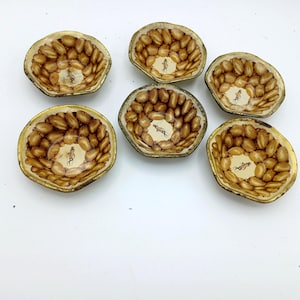May include: Six decorative, small, oval-shaped bowls. The bowls have a gold-colored rim and a brown and tan interior design. Each bowl has a small illustration of a person on a horse in the center. The bowls are arranged on a white surface.