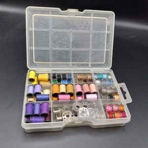 May include: A clear plastic storage box filled with spools of colorful thread and bobbins. The box has multiple compartments for organizing sewing supplies.