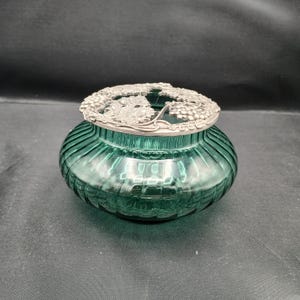 Peut inclure: Un pot en verre vert avec un couvercle en argent orné d'un motif de vigne. Le pot a une texture côtelée et est parfait pour ranger de petits objets.