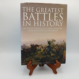 May include: A hardcover book titled The Greatest Battles in History: An Encyclopedia of Classic Warfare from Megiddo to Waterloo, edited by Jack Watkins. The cover features a detailed historical painting of a battlefield with soldiers on horseback.