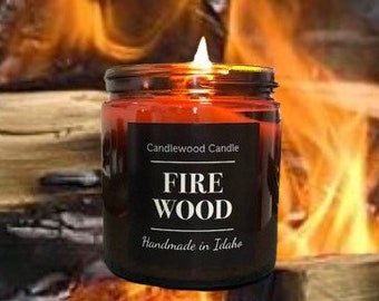 Puede incluir: Un tarro de vela de vidrio marrón con una etiqueta negra que dice "Candlewood Candle Fire Wood Handmade in Idaho". La vela está encendida y la llama es visible.