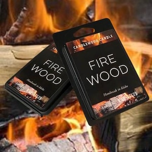 May include: Two black candle boxes with a white label that reads "Fire Wood" and "Candlewood Candle". The boxes are sitting on a piece of wood with flames in the background.