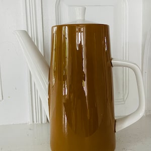 May include: A brown ceramic coffee pot with a white lid and handle. The pot has a glossy finish.