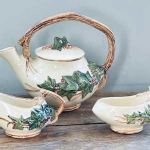May include: A vintage tea set with a teapot, creamer, and sugar bowl. The set is decorated with a leafy ivy pattern in shades of green, brown, and white.