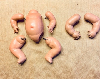 May include: A set of six porcelain doll parts, including the torso, two arms, and two legs. The parts are all in a pale pink color and have a smooth, glossy finish. The parts are designed to be assembled into a complete doll.