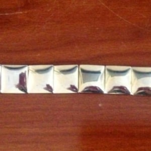 May include: A silver bracelet with a series of square-shaped links.