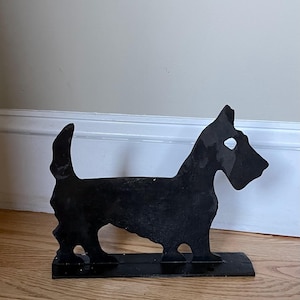 May include: Black metal silhouette of a Scottish terrier dog doorstop. The dog is standing on a black metal base.