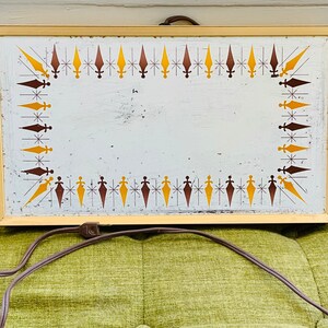 May include: A vintage electric warming tray with a white surface and a gold frame. The tray has a decorative border of brown and yellow stylized arrows. The tray is connected to a cord.