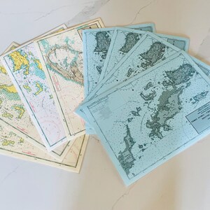 May include: A set of vintage nautical charts, some are blue and some are cream colored. The charts are folded and show a map of a coastline with islands and inlets. The charts are labeled with the text "TOPOGRAPHICAL SURVEY OF THE BRITISH VIRGIN ISLANDS".