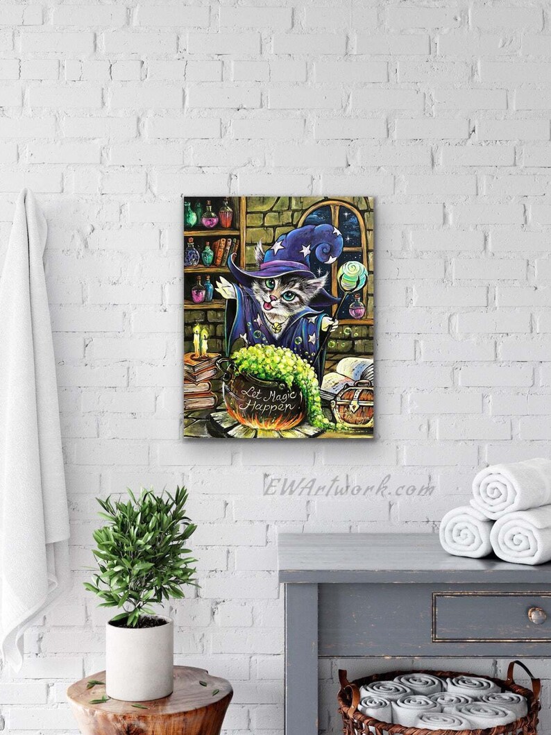 May include: A gray and white cat wearing a blue and purple wizard hat with stars and a pointed hat. The cat is holding a wand and is standing in front of a cauldron with green liquid. The cauldron is on a table with books, a chest, and a candle. The text "Let Magic Happen" is written on the cauldron.