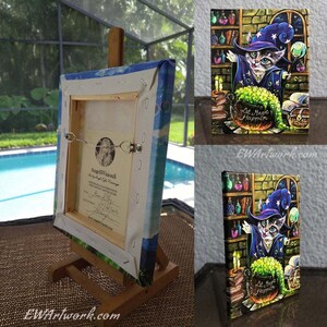 May include: A painting of a cat wearing a wizard hat and robe, stirring a cauldron with a wand. The cat is surrounded by books, potions, and a chest. The text "Let Magic Happen" is written on the cauldron. The painting is on a canvas and is framed.