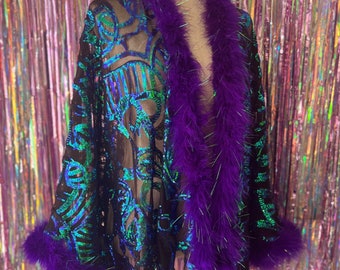 Op de afbeelding: Een zwarte, doorschijnende kimono met iriserende pailletten en een paarse verenbies. De kimono heeft een lange, vloeiende silhouet en is perfect om elke outfit een vleugje glamour te geven.