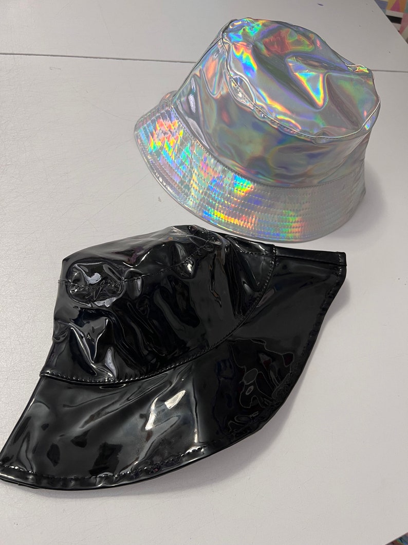K&ouml;nnte beinhalten: Zwei Bucket-Hats, einer silberfarben mit holografischem Finish und einer schwarz mit gl&auml;nzendem Finish.