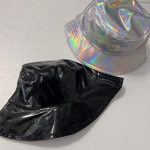 K&ouml;nnte beinhalten: Zwei Bucket-Hats, einer schwarz und einer silber mit holografischem Finish.