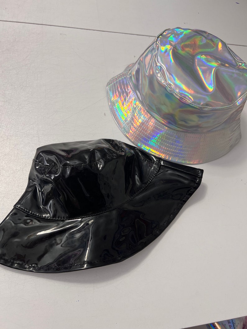 K&ouml;nnte beinhalten: Zwei Bucket-Hats, einer schwarz und einer silber mit holografischem Finish.