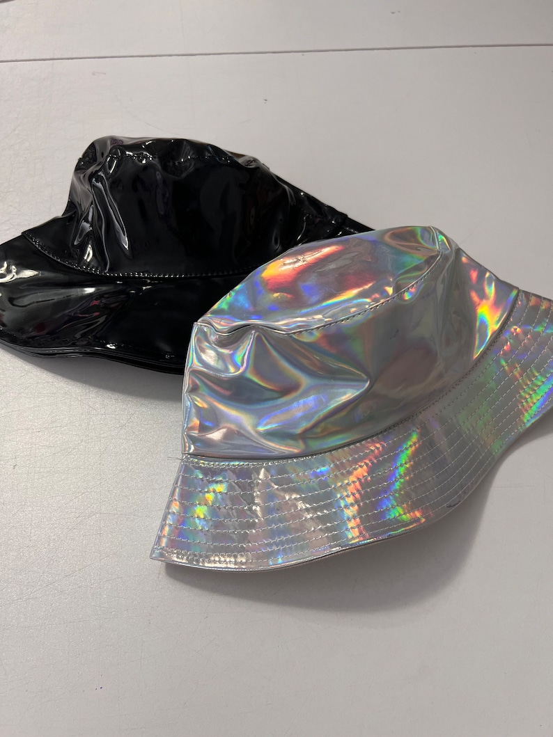 K&ouml;nnte beinhalten: Zwei Bucket-Hats, einer schwarz und einer silber mit holografischem Finish.