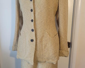 May include: A beige tweed suit comprising a skirt and a jacket. The jacket features a notched collar, a button-up front, and two flap pockets. The skirt is knee-length and has a straight silhouette.
