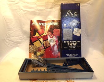 May include: A Lily Speed-O-Weave Twin adjustable loom kit featuring a blue box with white text, an instruction booklet showing a person wearing a crocheted garment, and blue metal loom components stored in a rectangular cardboard tray.