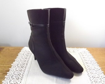 May include: A pair of black ankle boots with a pointed toe and a small heel. The boots have a strap and buckle detail around the ankle. The boots are made of a smooth, matte material.