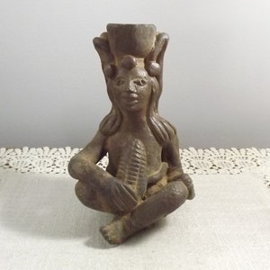 May include: A brown ceramic figurine of a seated figure with a headdress and a leaf in its hand.