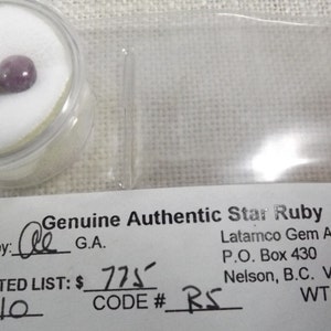 May include: Two small, pink star rubies in a clear plastic container. The container is labelled "Genuine Authentic Star Ruby" and includes the text "Certified by: de G.A. SUGGESTED LIST: £775 LOT# 10 CODE # RS WT: 4.10 ct."