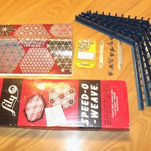 May include: A vintage Lily Speed-O-Weave kit with a red box and the text "SPEED-O-WEAVE". Includes a blue corner weaving frame, weaving tools, and a booklet with geometric patterns. The kit is on a wooden surface.
