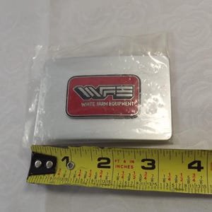 May include: A silver metal rectangle with a red rectangle inside. The red rectangle has the text "WFE" in white and the text "WHITE FARM EQUIPMENT" in black.