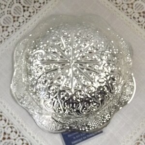 Puede incluir: Un cuenco de plata con un intrincado dise&ntilde;o floral. El cuenco tiene un borde festoneado y est&aacute; hecho de metal.