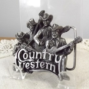 K&ouml;nnte beinhalten: Silberne G&uuml;rtelschnalle mit einer Gruppe von vier Musikern, die Instrumente spielen. Die Schnalle tr&auml;gt die Aufschrift "Country Western".