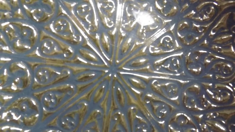 Puede incluir: Primer plano de un plato decorativo con acabado met&aacute;lico plateado y dorado. El plato tiene un dise&ntilde;o intrincado en relieve que se asemeja a una flor o una estrella.
