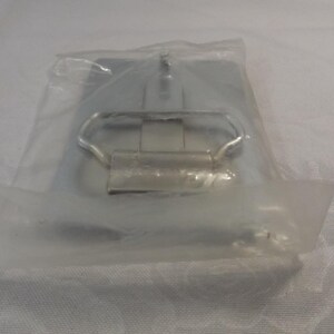 May include: A silver metal belt buckle with a simple design. The buckle is packaged in a clear plastic bag.