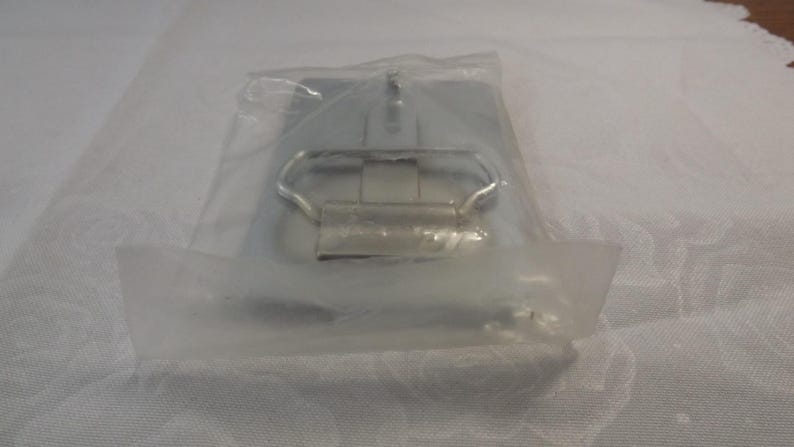 May include: A silver metal belt buckle with a simple design. The buckle is packaged in a clear plastic bag.